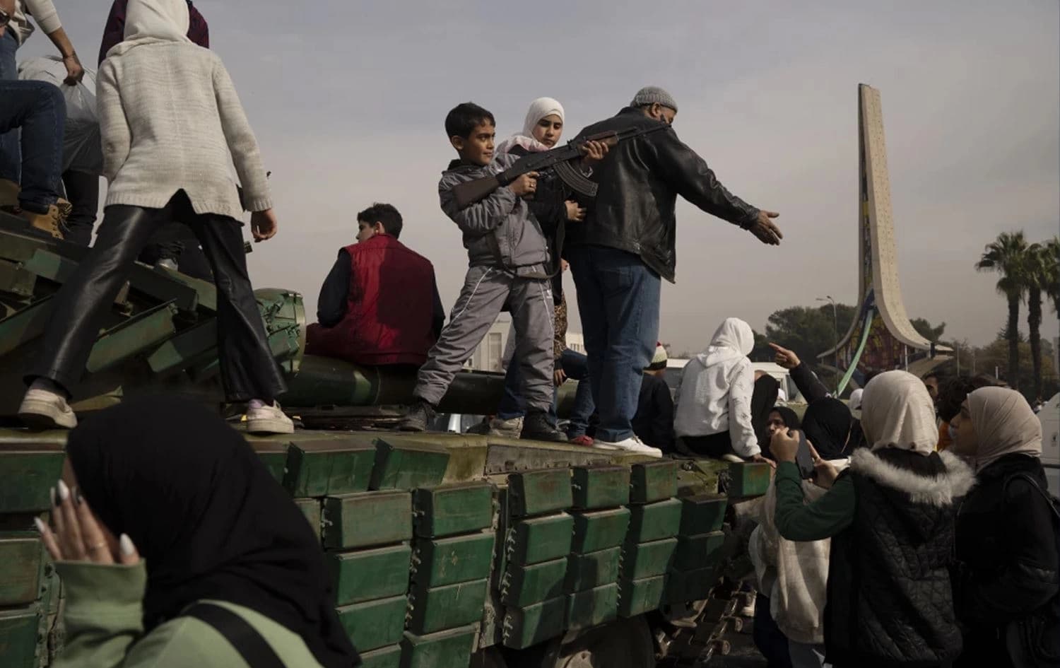 A boy holding a rifle borrowed from a Syrian rebel standing on top of a tank of the fallen regime at the Umayyad Square in Damascus, Syria on December 11, 2024. Photo: Leo Correa/AP