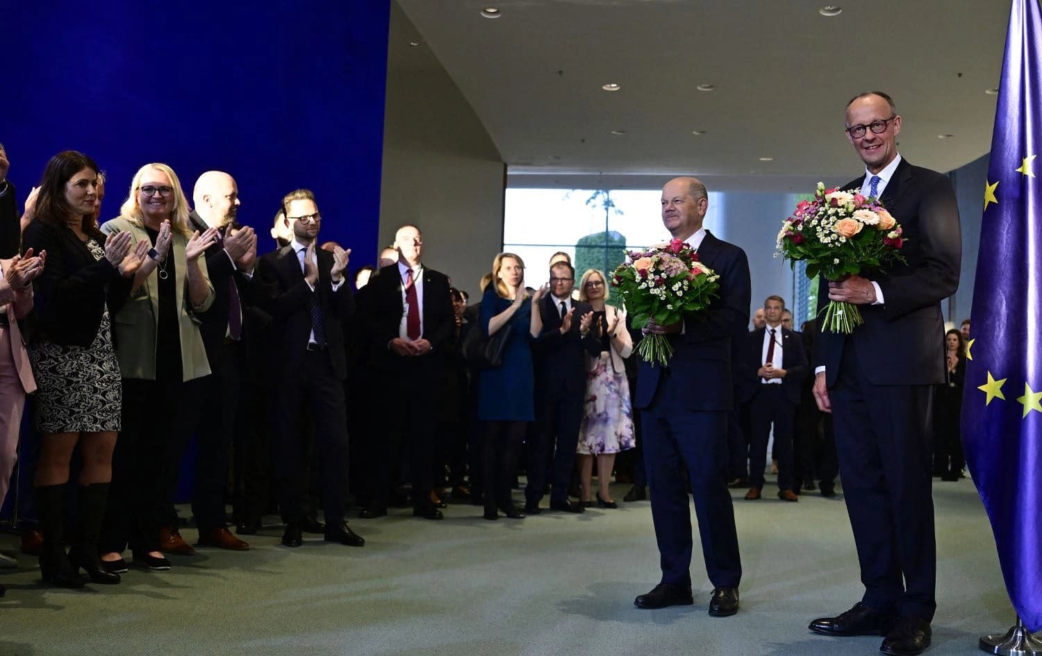 Newly elected German Chancellor Friedrich Merz (R) and his predecessor Olaf Scholz pose with bouquets of flowers they were presented with by chancellery employees during a handover ceremony at the Chancellery in Berlin on May 6, 2025. Photo: John Macdougall/AFP