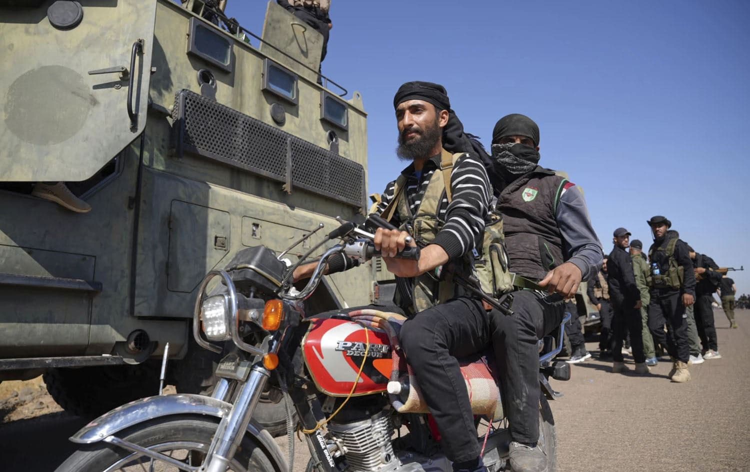 Two fighters from the Sunni Bedouin clans, ride their motorcycle as they pass by Syrian government security forces deployed on the outskirts of the Suwayda province where clashes erupted between Druze militias and Sunni Bedouin clans, southern Syria, Monday, July 14, 2025. Photo: Malek Khattab/AP