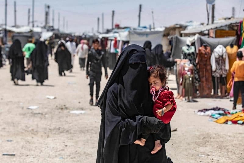 A woman carries a child as she walks through Syria's al-Hol camp. AFP file photo