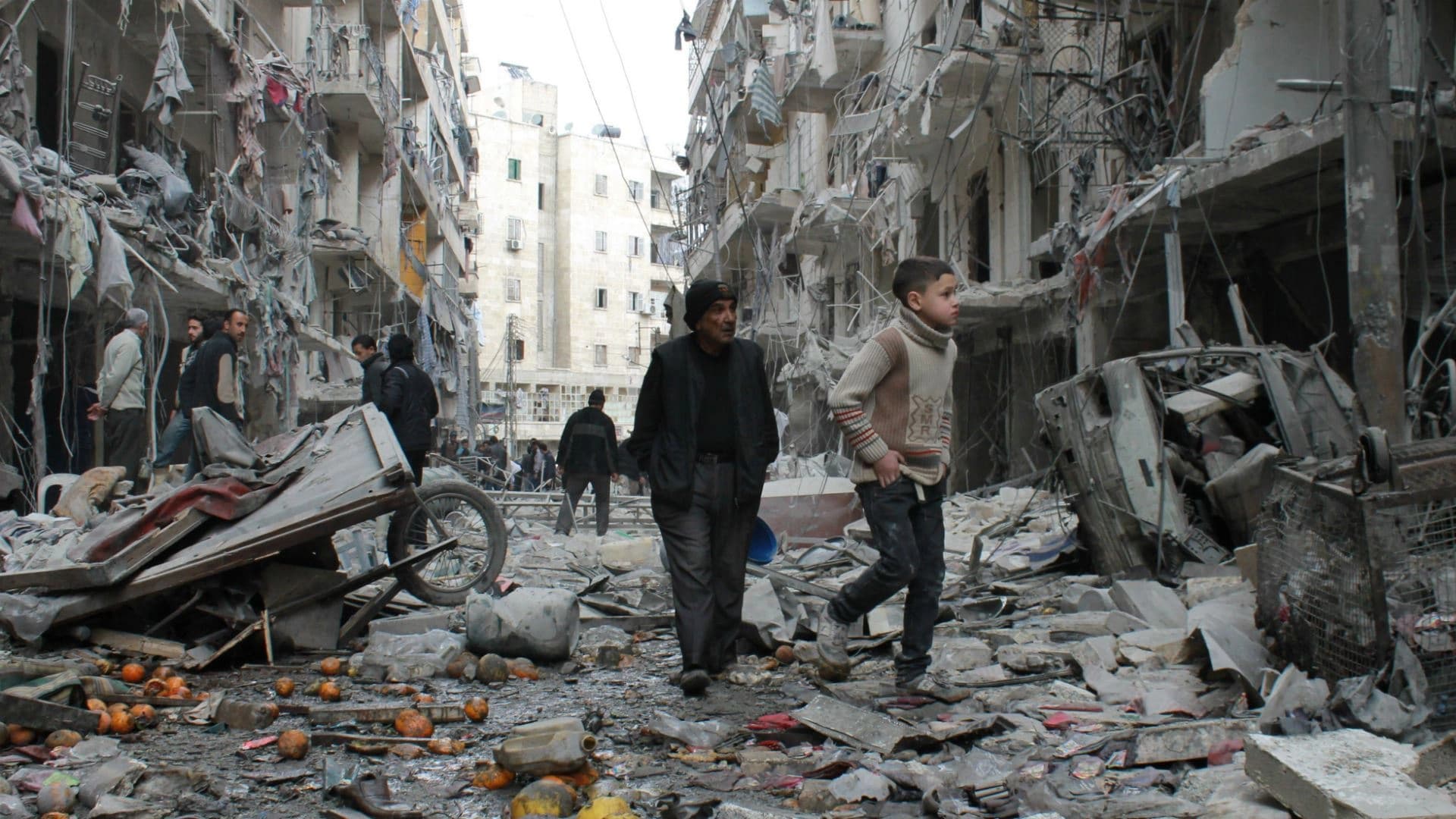 An elderly man and a child walk amidst debris in a residential block hit by explosives in Syria's northern Aleppo province. Photo: AFP