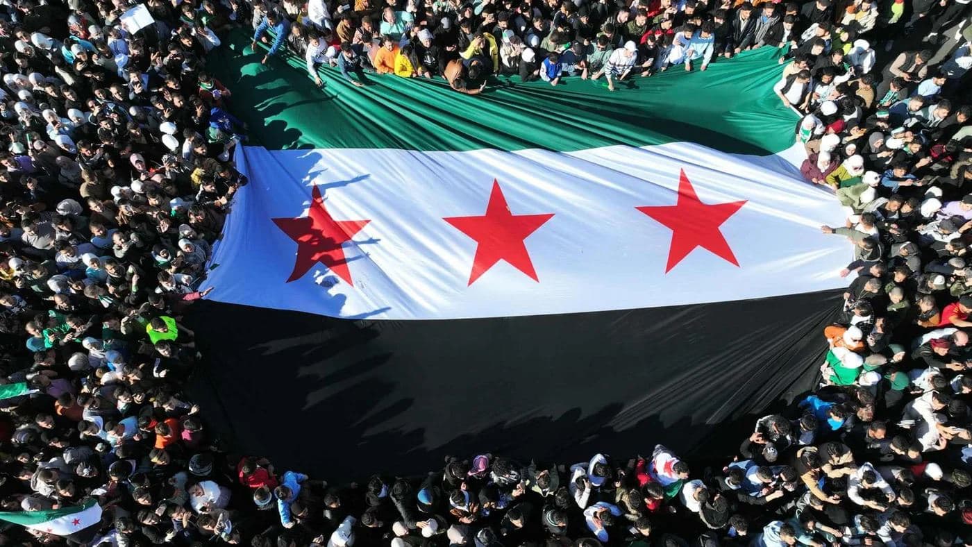 A giant Syrian revolutionary flag is unfurled by crowds gathered in Damascus' Omayyad Square on Friday 13 December 2024. AFP file photo
