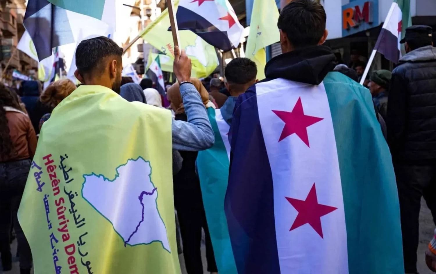 Two men carrying the SDF flag (left) and the Syrian flag (right) in the northeastern city of Qamishli, on December 19, 2024. Photo: Delil Souleiman/AFP