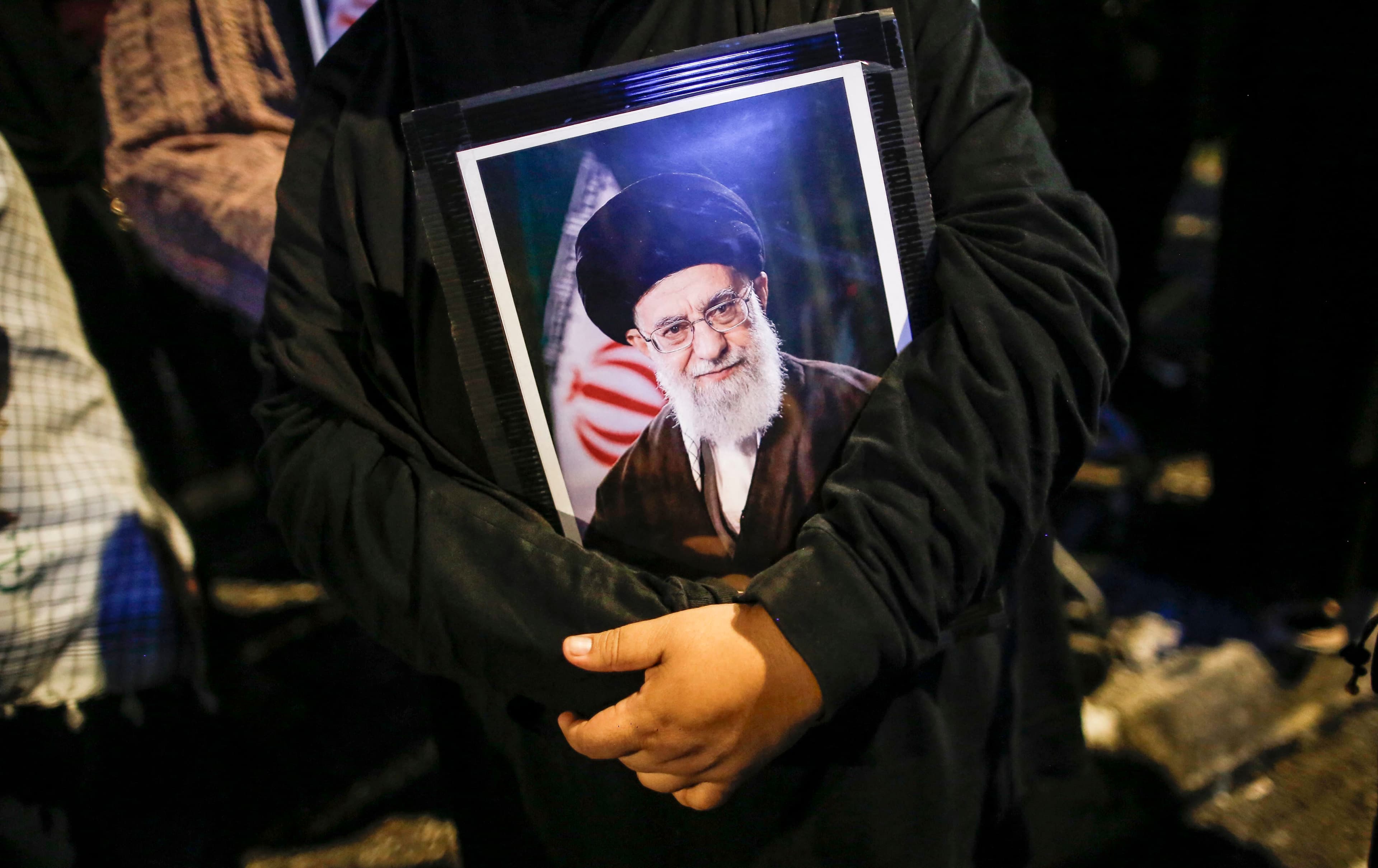 خانمێک لەبەردەم باڵیۆزخانەی ئەمریکا لە کوالالامپوور وێنەی عەلی خامنەیی، رێبەری کۆچکردووی کۆماری ئیسلامیی لە دەست گرتووە. رۆژی 1ـی ئاداری 2026. وێنە: AFP