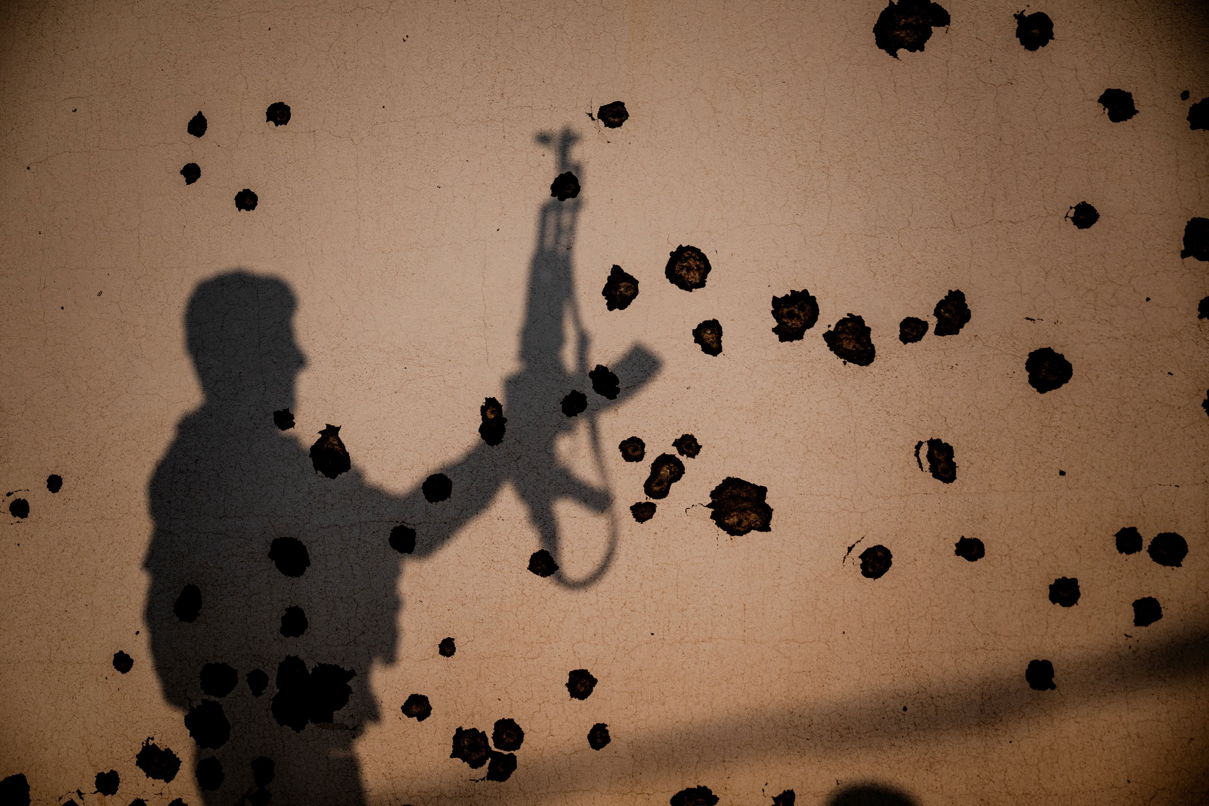 The shadow of a Kurdish fighter, a member of the Organization of Iranian Kurdistan Struggle (Sazmani Khabat), falls on the shrapnel scarred wall of a damaged building, following an Iranian drone attack to their base near Erbil on March 9, 2026. AFP photo