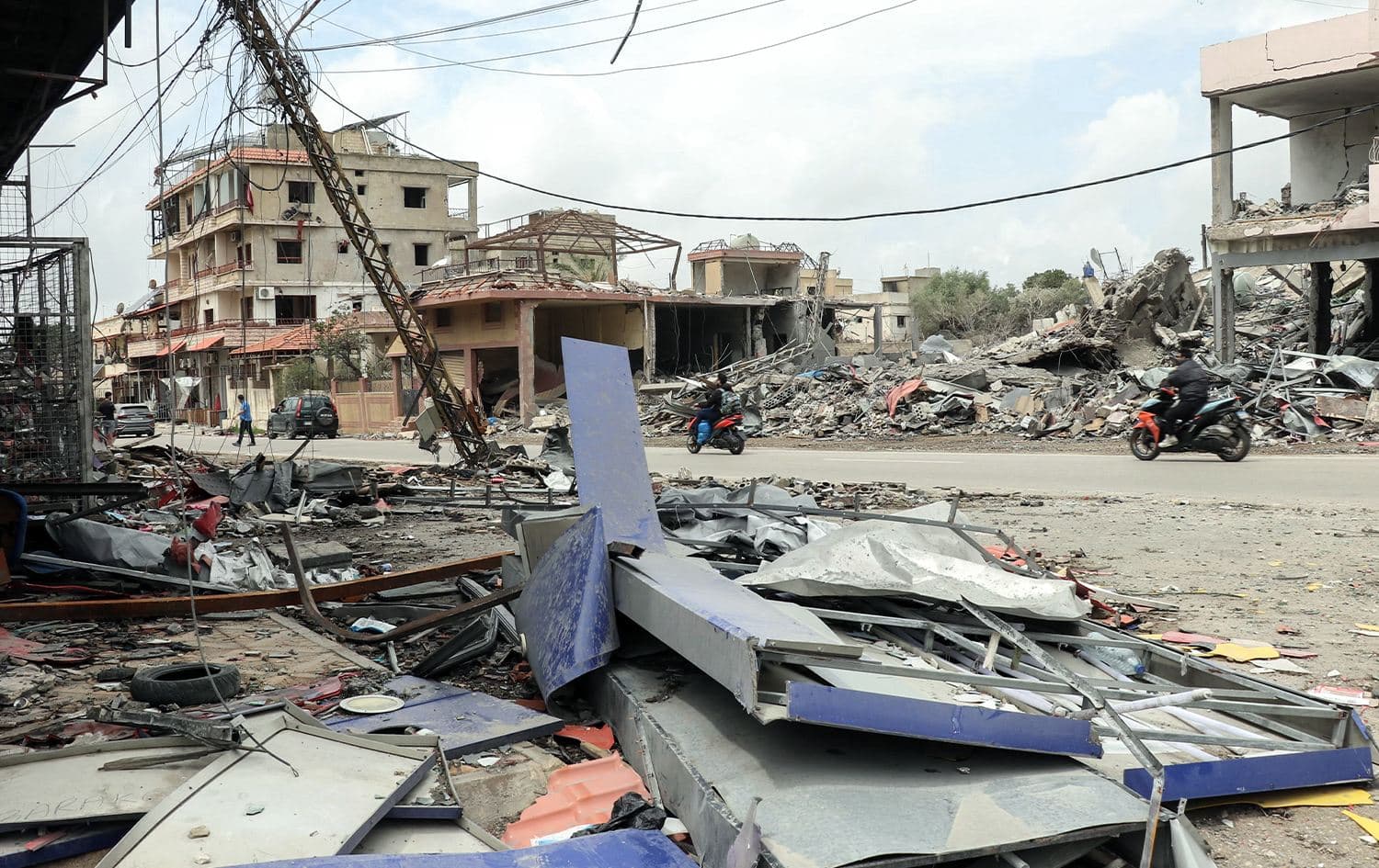 People riding mopeds drive past destroyed buildings as displaced residents return to the southern Lebanese village of Srifa on April 19, 2026. Photo: Kawnat Haju / AFP