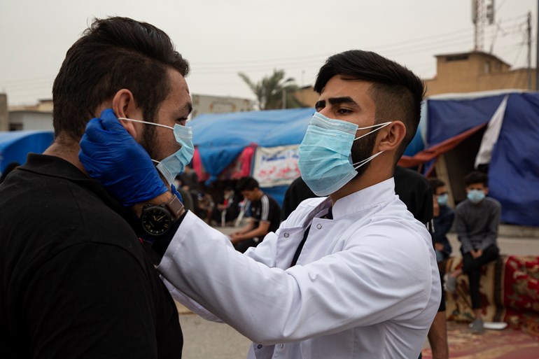 An Iraqi student shows an anti-government demonstrator how to wear a protective mask against the coronavirus during a rally in the southern city of Basra on February 25, 2020. Photo: Huseein Faleh / AFP