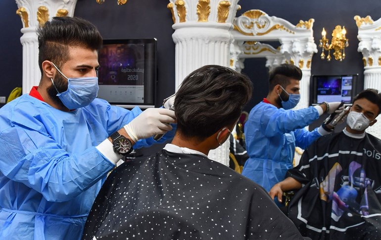 A hairdresser cuts the hair of a costumer while wearing protective clothing due to the spread of the COVID-19 coronavirus, in the southern Iraqi city of Nasiriyah on March 28, 2020. Photo: Asaad Niazi/ AFP