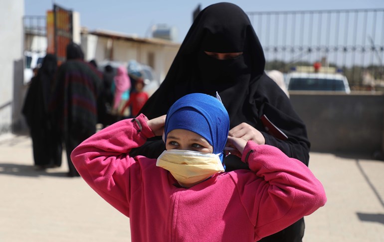 A Syrian woman sets a protective mask on a child's face in a camp for displaced persons in Idlib province on March 23, 2020. Photo: Aaref Watad/AFP