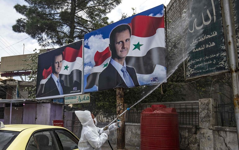 A member of the disinfection units of the semi-autonomous Syrian Kurdish administration sprays billboards, including some of President Bashar al-Assad, in Qamishli on March 24, 2020. Photo: Delil Souleiman/AFP