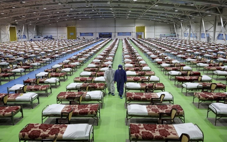 People in protective clothing walk past rows of beds at a temporary hospital at the international exhibition center in northern Tehran on Thursday, March 26, 2020. Photo: Ebrahim Noroozi/AP