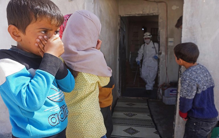 Syrian children watch a member of the Syrian civil defence, known as the White Helmets, disinfecting a former school building in Idlib province on March 26, 2020. Photo: Muhammad Haj Kadour/AFP