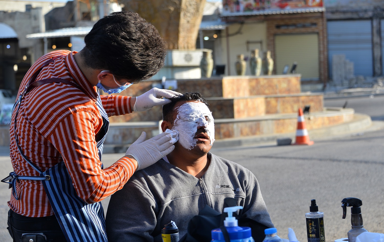 An Iraqi hairdresser, wearing personal protective equipment, provides a facial mask to a member of the security forces during the coronavirus (COVID-19) pandemic in the northern Iraqi city of Mosul on April 18, 2020. Zaid Al-Obeidi/ AFP