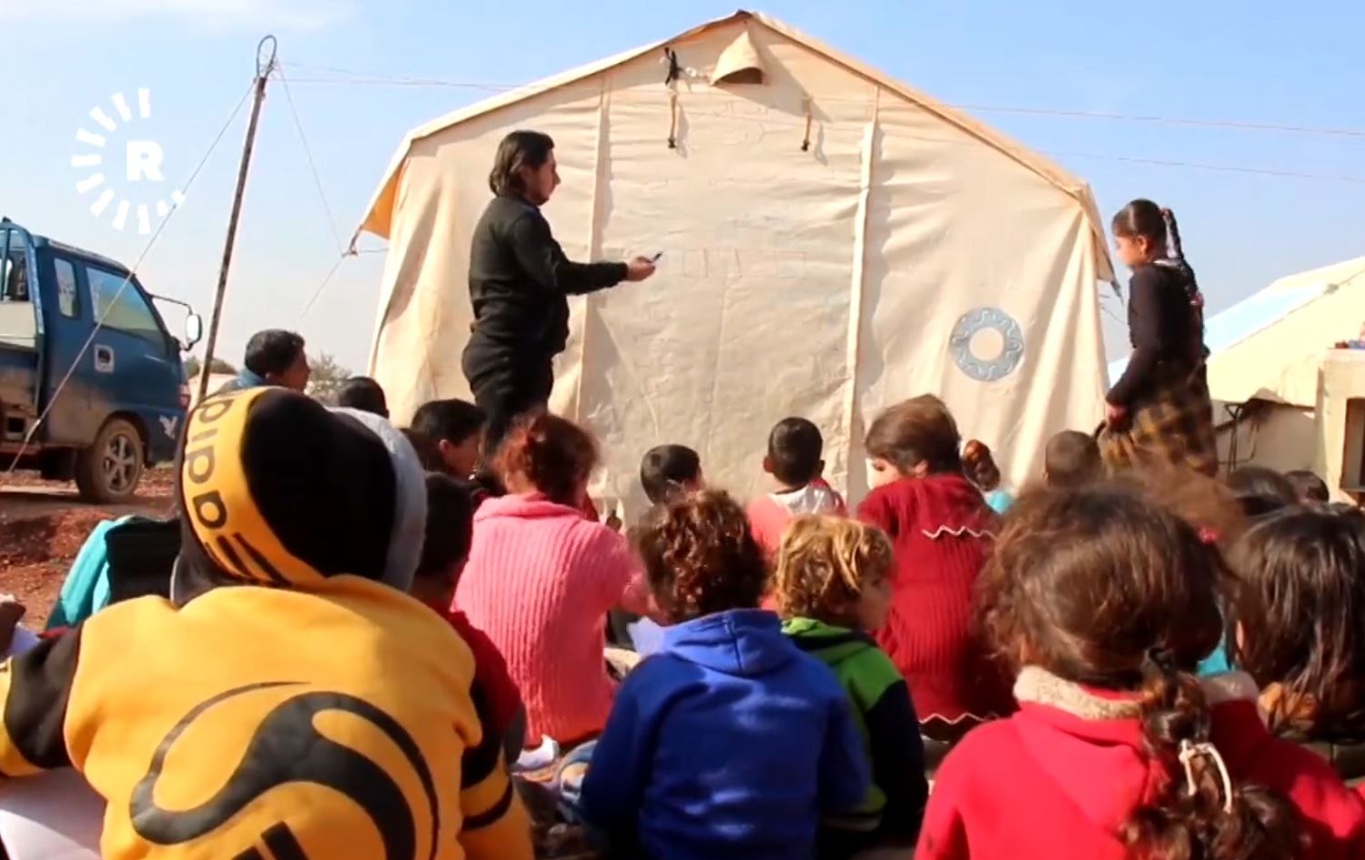 Koçberekî Sûrî zarokên kampekê fêrî nivîsandin û xwendinê dike