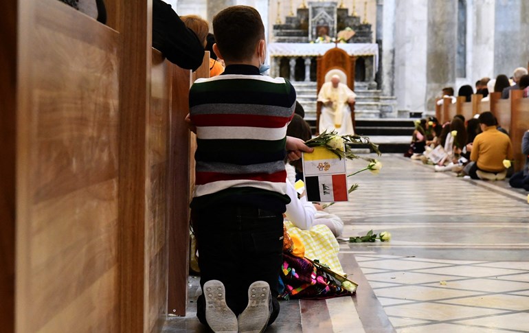 A child kneels on the floor along the nave while Pope Francis (background) sits on the throne at the Syriac Catholic Church of the Immaculate Conception (al-Tahira-al-Kubra) in Qaraqosh (Baghdeda), Nineveh province on March 7, 2021. Photo: Vincenzo Pinto/AFP