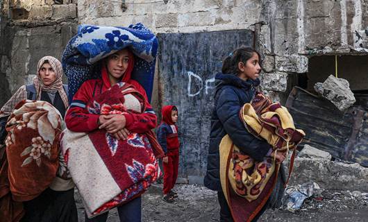 نساء من غزة يحملن بطانيات أثناء مرورهن بجوار منازل مدمرة/ AFP