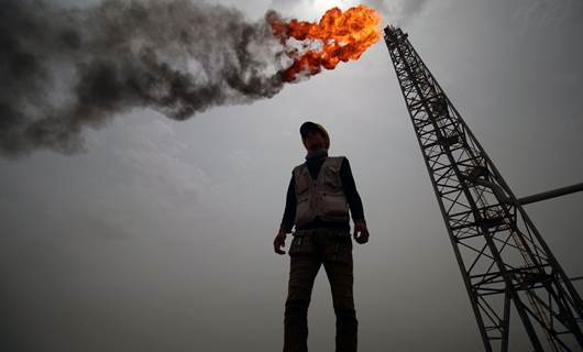 کارمەندێکی کۆمپانیای نەوتیی لە عێراق کە گڕی ئاگری نەوتەکە لە پشتییەوە دەبینرێت، وێنە: AFP