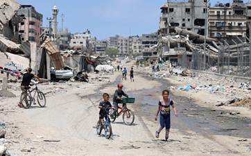 أطفال فلسطينيون يركبون دراجاتهم على طول شارع دمره القصف الإسرائيلي في مدينة غزة -AFP