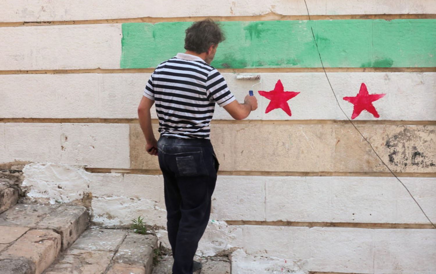 Suriyeli bir vatandaş ülkesinin yeni bayrağını duvara çiziyor Foto: AP
