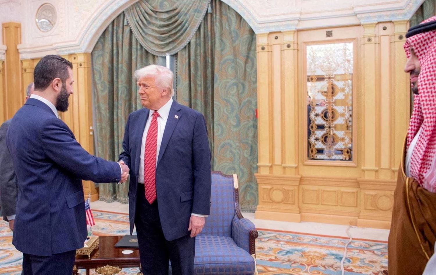  دۆناڵد ترەمپ و ئەحمەد شەرع تەوقە دەکەن و محەممەد بن سەلمانیش لەلایان وەستاوە. 