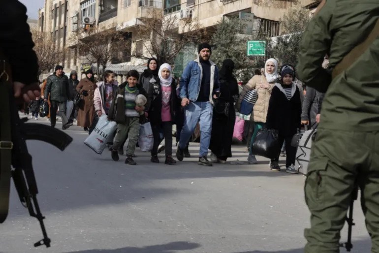 Children carrying belongings walk past security forces as residents flee Aleppo’s Ashrafieh neighbourhood. Photo: AFP