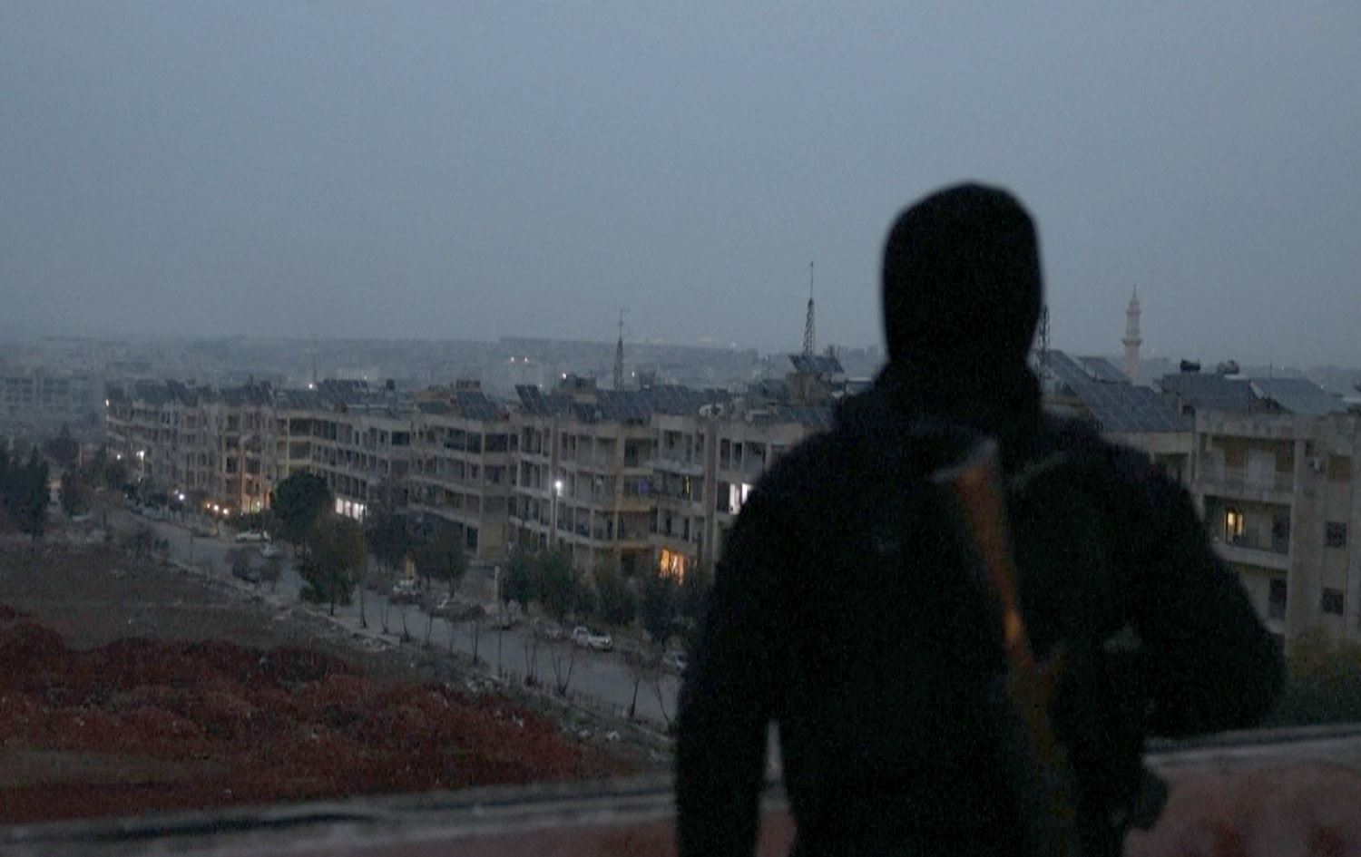 کەسێک لە گەڕەکێکی حەلەب بە چەکەوە وەستاوە و لەو ناوچانە دەڕوانێت کە شەڕ و ئاڵۆزییان تێدایە. وێنە: AFP