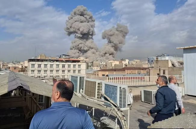 خەڵکی لە سەربانی ماڵەکانیانەوە دەڕواننە شارەکە، دوای هێرشە ئاسمانییەکانی سەر تاران لە 28y شوباتی 2026. وێنە: AP