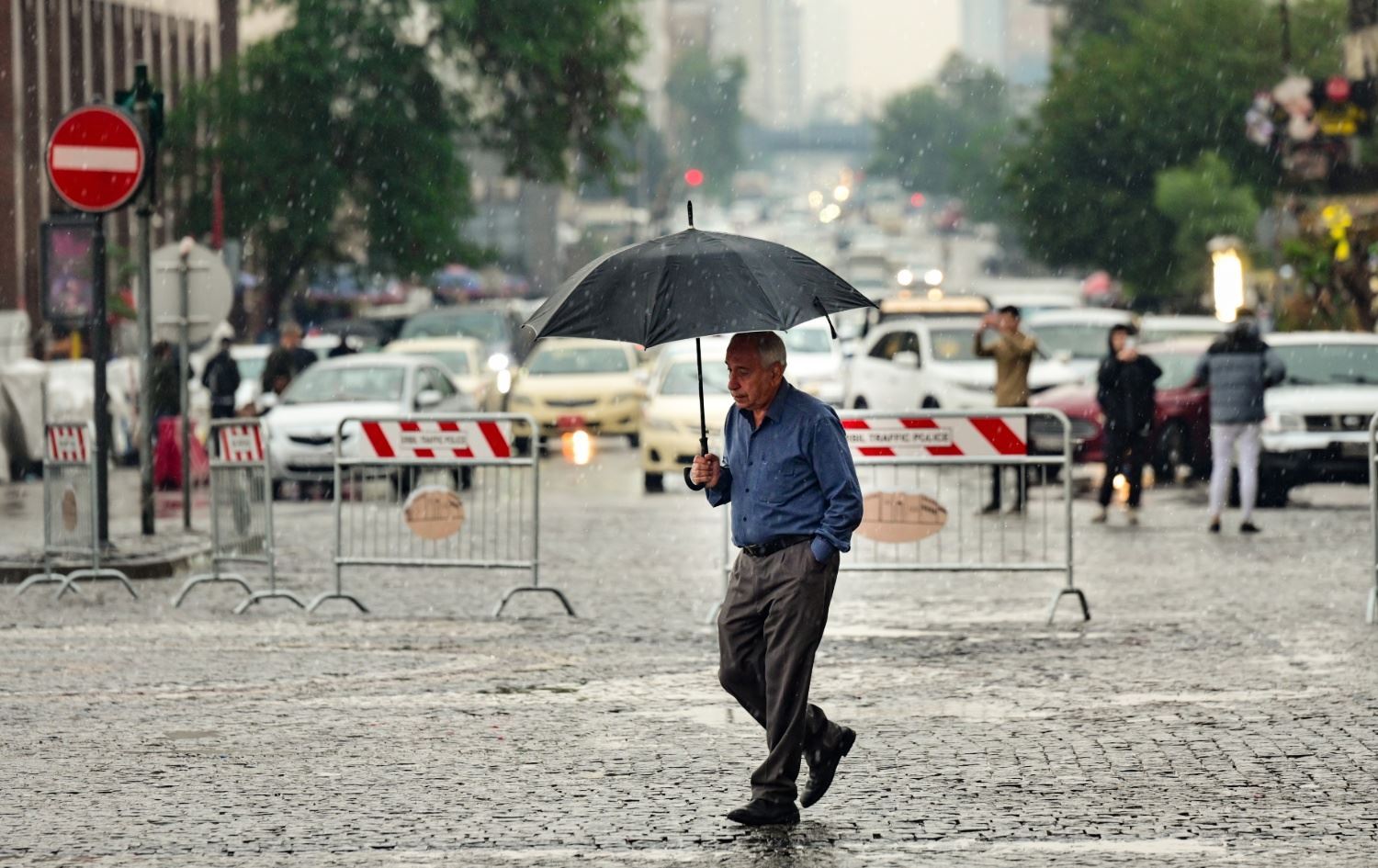 هاونیشتمانییەک لە سەنتەری شاری هەولێر بە چەترەوە لە ژێر باراندا رێ دەکات. وێنە: بڵند تاهیر 