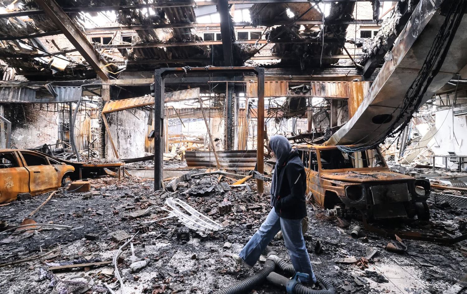 رۆژنامەنووسێک لە نێو پاشماوەی تێکشکاوی ئۆتۆمبێلە بۆردوومانکراوەکاندا لە ناوەندێکی چاککردنەوەی ئۆتۆمبێل لە رۆژهەڵاتی تاران. وێنە: AFP