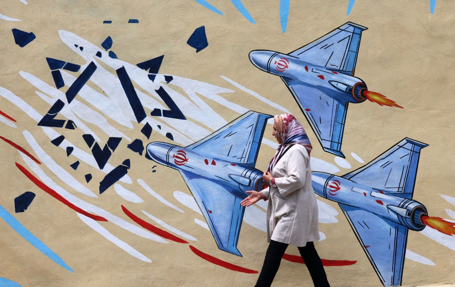  ئافرەتێک بە تەنیشت دیوارێکدا تێدەپەڕێت کە دروشمی دژ بە ئەمریکا و ئیسرائیلی لەسەر کێشراوە. وێنە: AFP