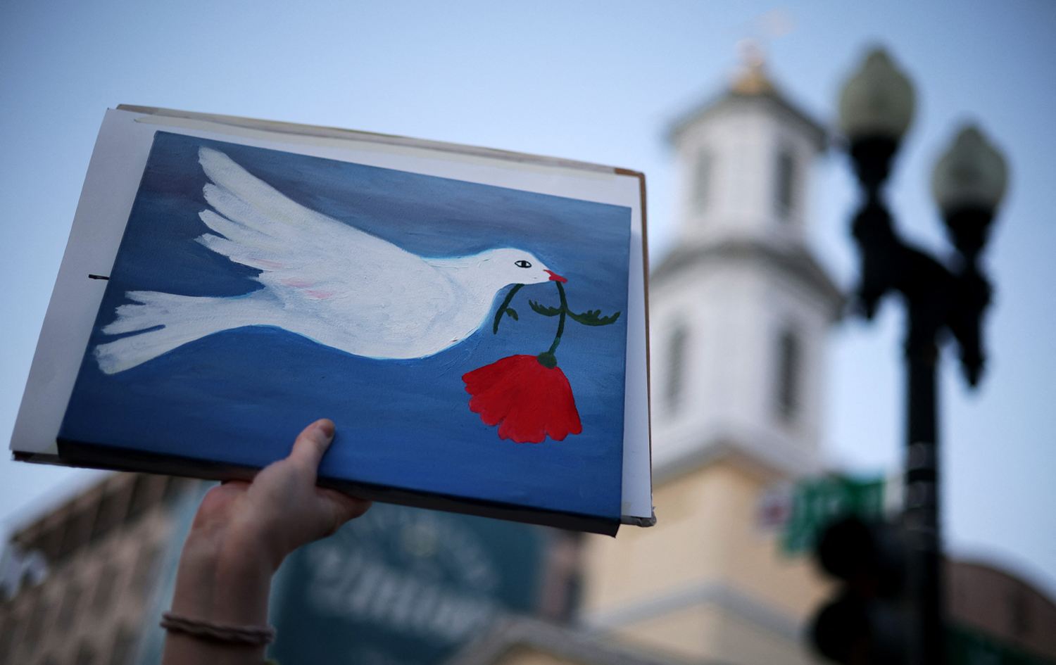 خۆپێشاندەرێک لە بەردەم کۆشکی سپی وێنەی کۆترێکی وەکو هێمای ئاشتی بەرزکردووەتەوە. وێنە: AFP